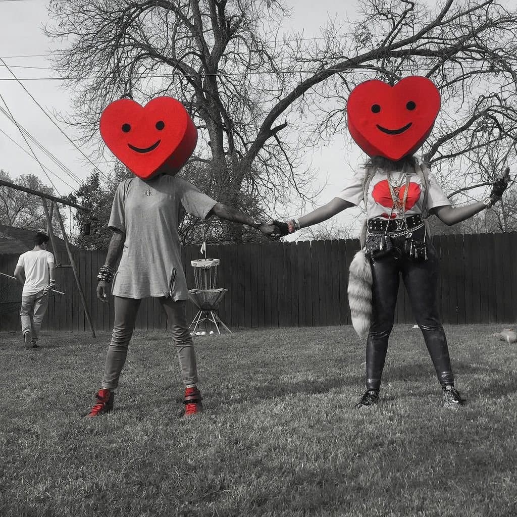 Two people in heart-shaped masks holding hands in a backyard.